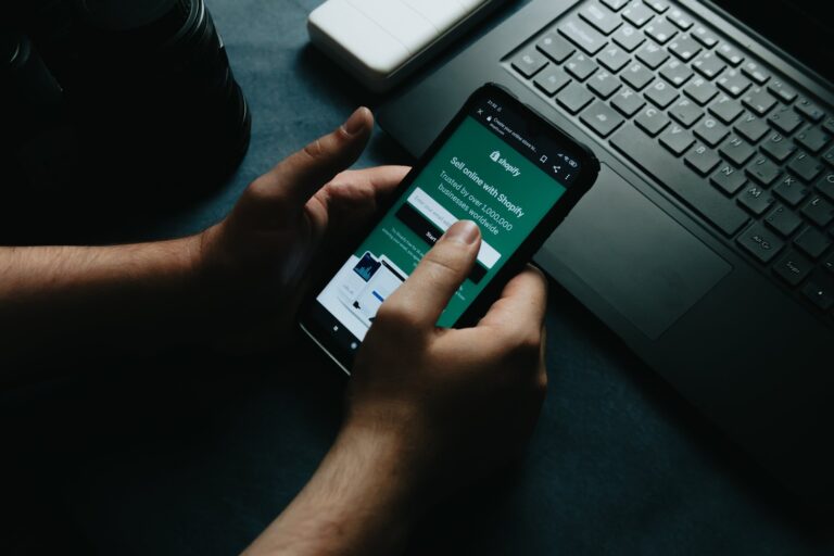 A hand holding a phone showing the Shopify home page, illustrating Shopify DotDev 2026 platform updates